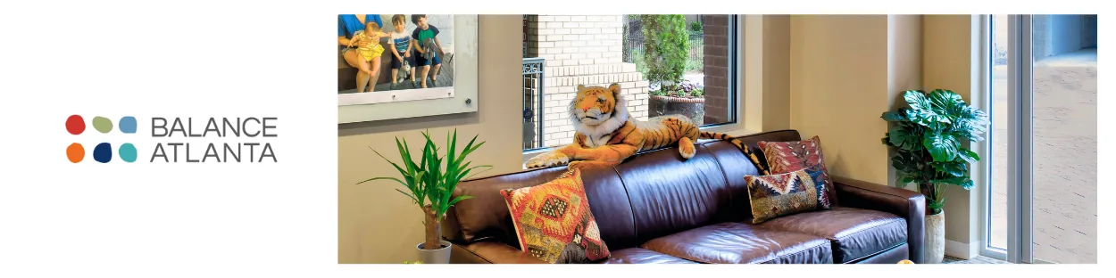 Balance Atlanta logo beside a waiting room with a brown leather sofa, colorful throw pillows, a plush tiger on the sofa back, and potted plants by a window.