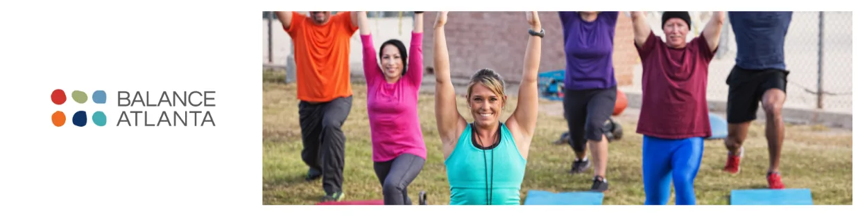 Outdoor group fitness class with instructor at center raising arms and participants behind doing lunges on exercise mats.