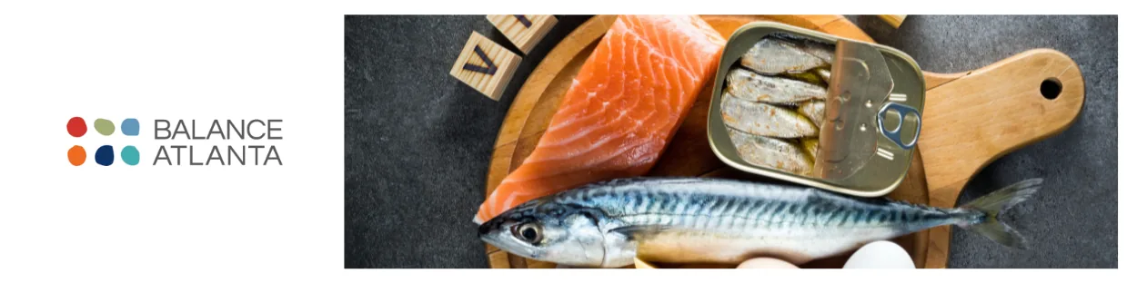 Balance Atlanta logo next to vitamin D–rich foods on a cutting board: salmon fillet, whole mackerel, open tin of sardines, and eggs