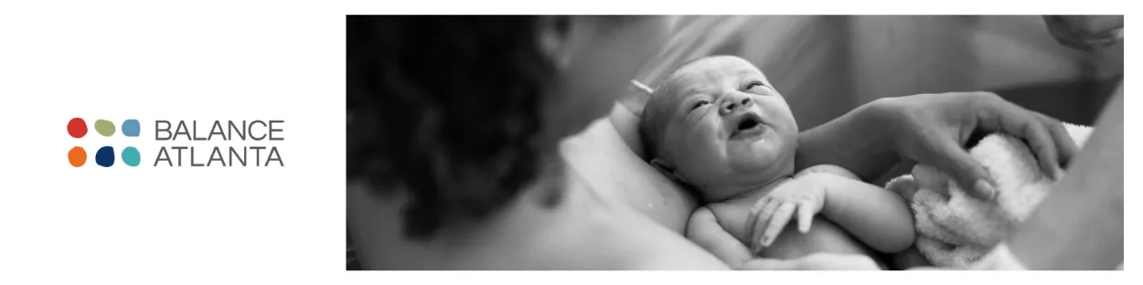 Black-and-white scene of a baby cradled against an adult's chest with a hand supporting the baby.