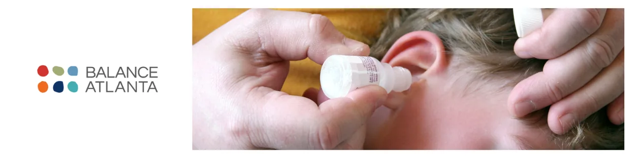 Adult hands applying ear drops to a child's ear with the Balance Atlanta logo at left.