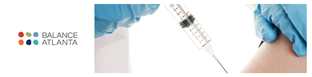 Gloved clinician preparing a syringe to inject medication into a patient's upper arm, with the Balance Atlanta logo at left.