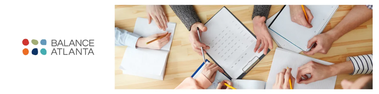 Hands of several people writing in notebooks and pointing at a clipboard calendar beside the Balance Atlanta logo