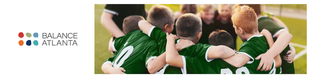Soccer team in green jerseys huddled together on a field, with a Balance Atlanta logo on a white panel at left.