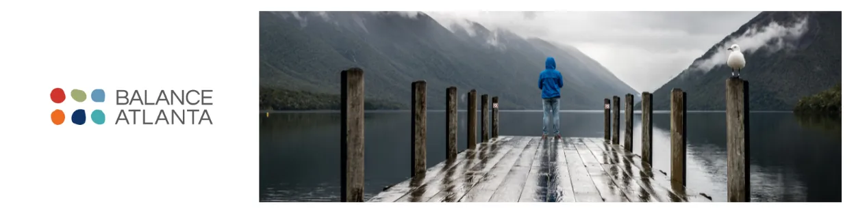 Balance Atlanta logo at left; a person in a blue jacket stands at the end of a wet wooden dock looking over a misty mountain lake, a seagull perched on a post.