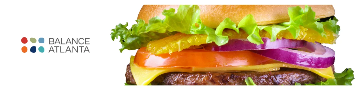 Close-up of a cheeseburger with lettuce, tomato, cheese, and sliced red onion beside the Balance Atlanta logo on a white background.