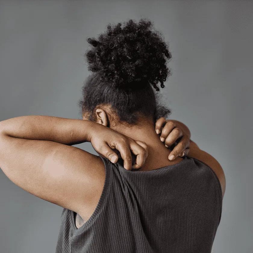 Person seen from behind scratching their neck and upper back.