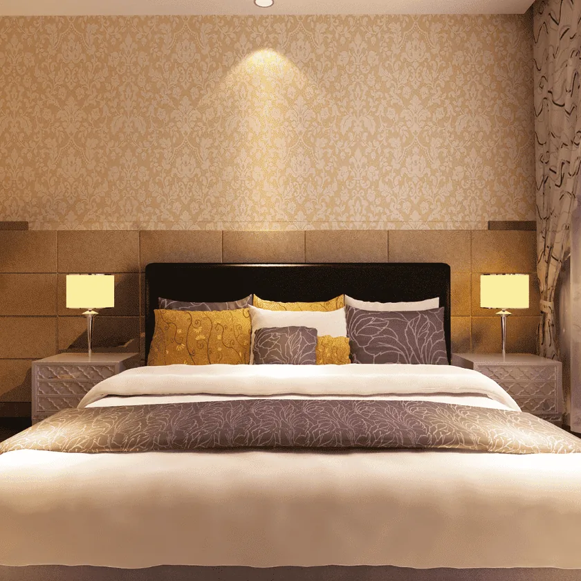 A cozy bedroom with a large made bed, patterned headboard, multiple decorative pillows, bedside lamps, and warm soft lighting.