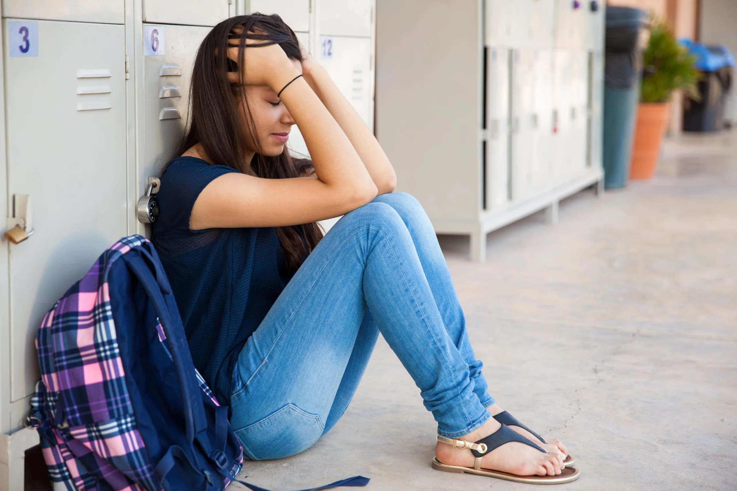 Student sitting on the floor by school lockers with hands holding their head and a backpack beside them