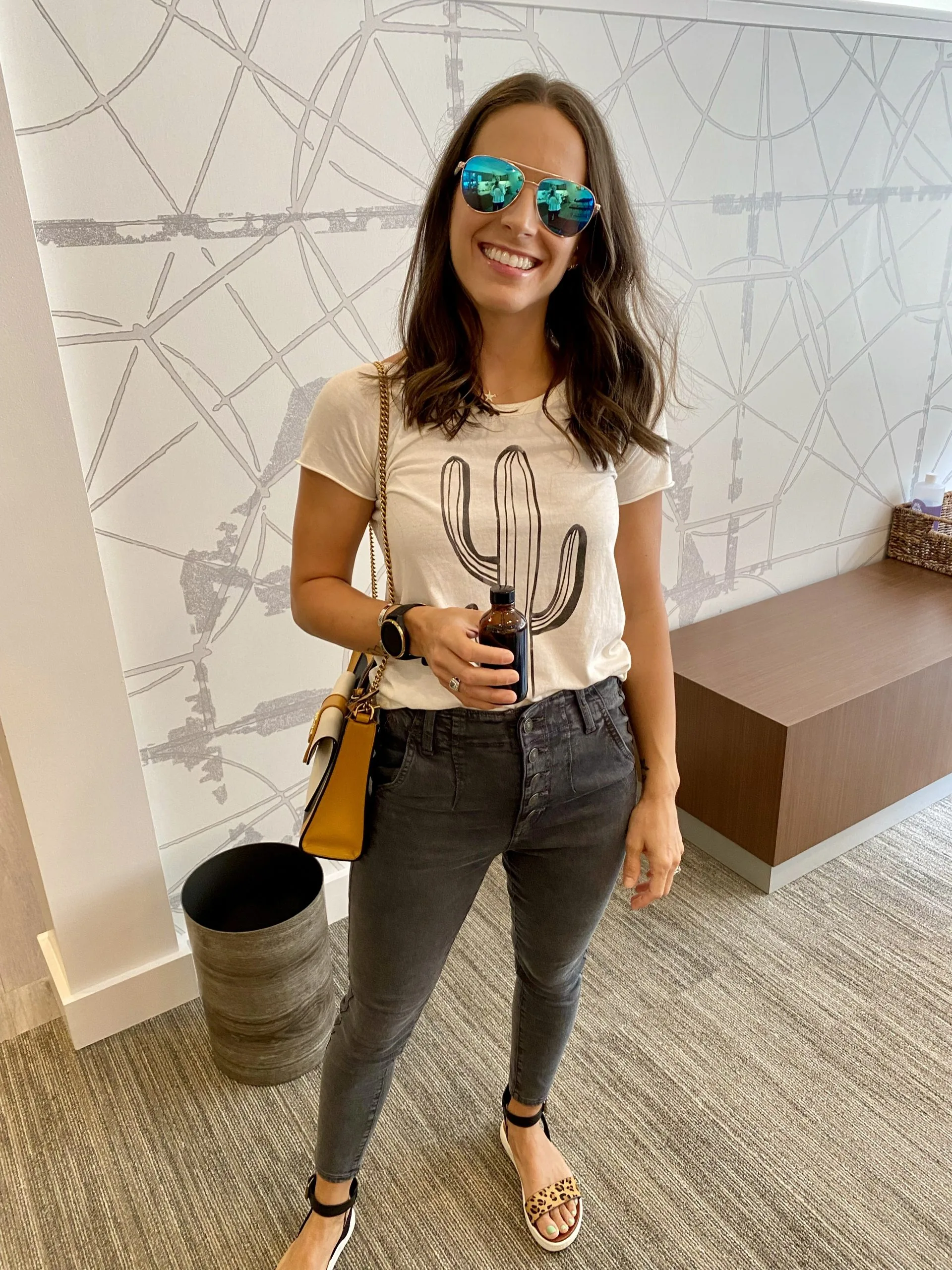 Woman wearing mirrored sunglasses holding a small brown bottle in a clinic reception area