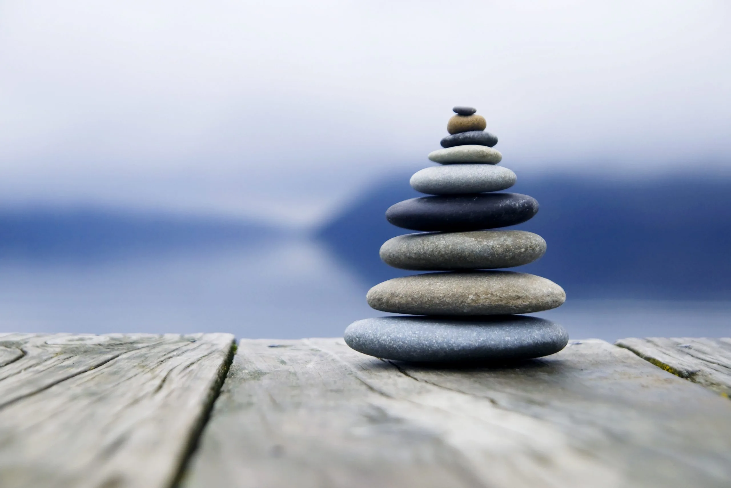Balanced stack of smooth pebbles on a weathered wooden dock with a misty lake and distant hills in the background