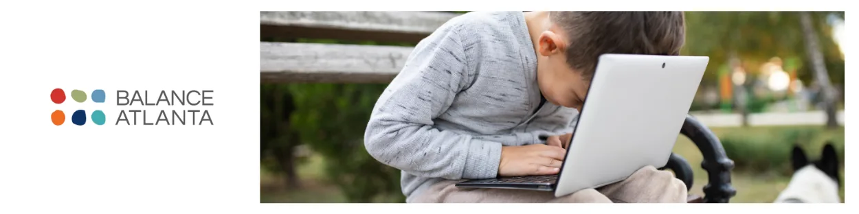 Child sitting on a park bench leaning forward while using a laptop, with the Balance Atlanta logo visible at left.