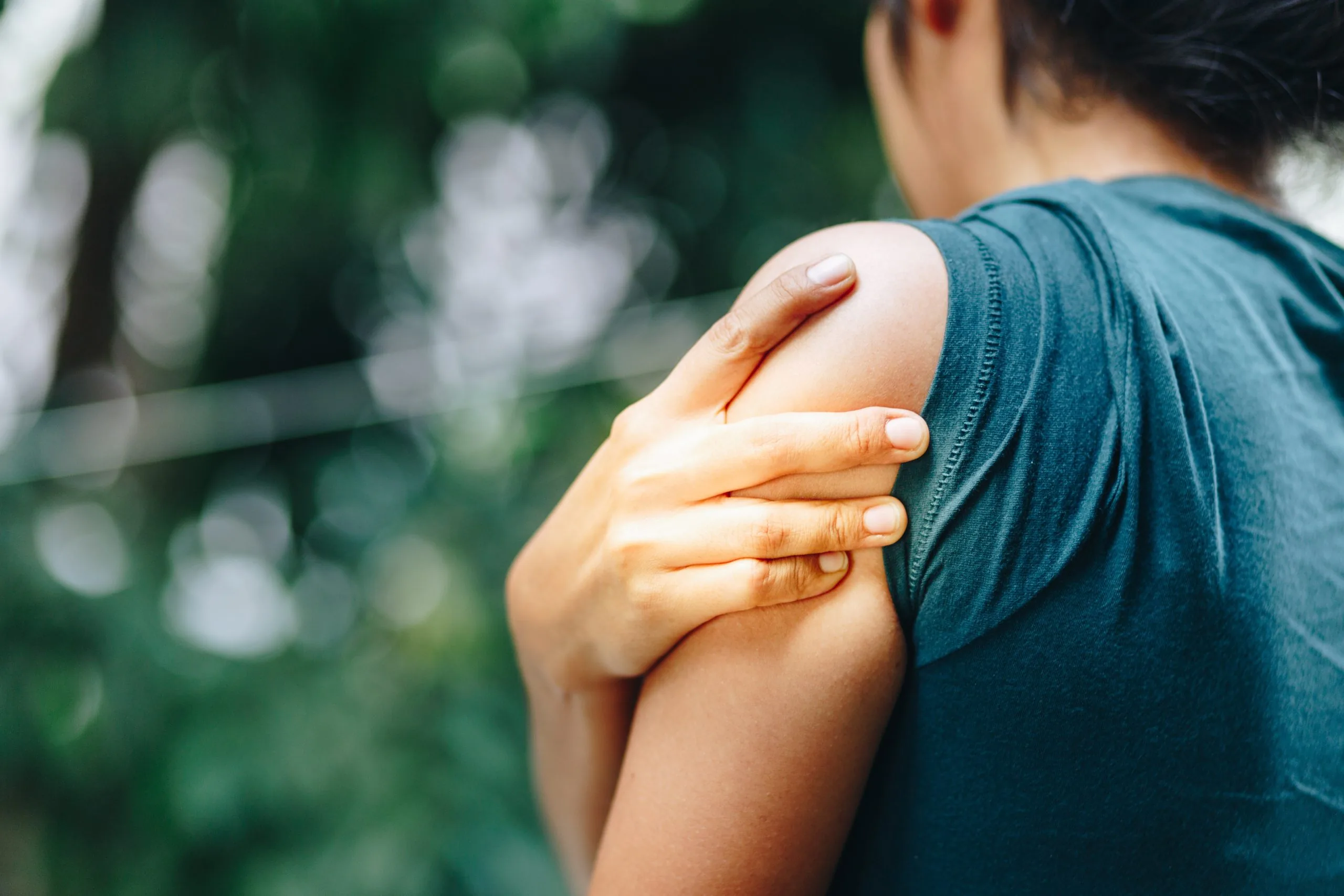 Person holding their upper arm near the shoulder with one hand, indicating arm pain.