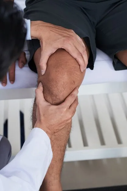 Clinician palpating a patient's knee during an exam to assess joint pain and mobility related to arthritis.