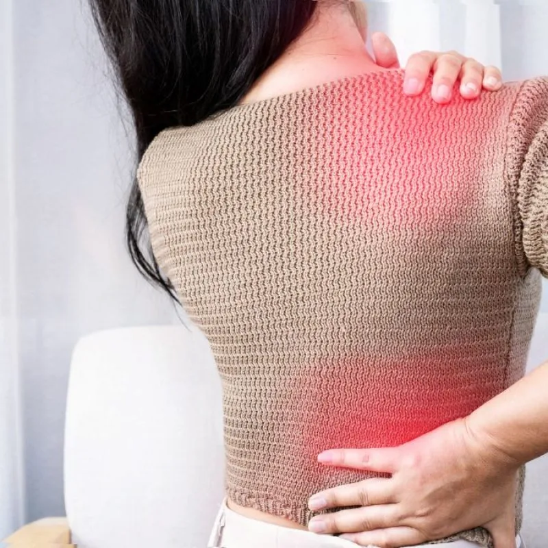 Person seen from behind holding upper and lower back with hands, red highlight indicating areas of back pain.