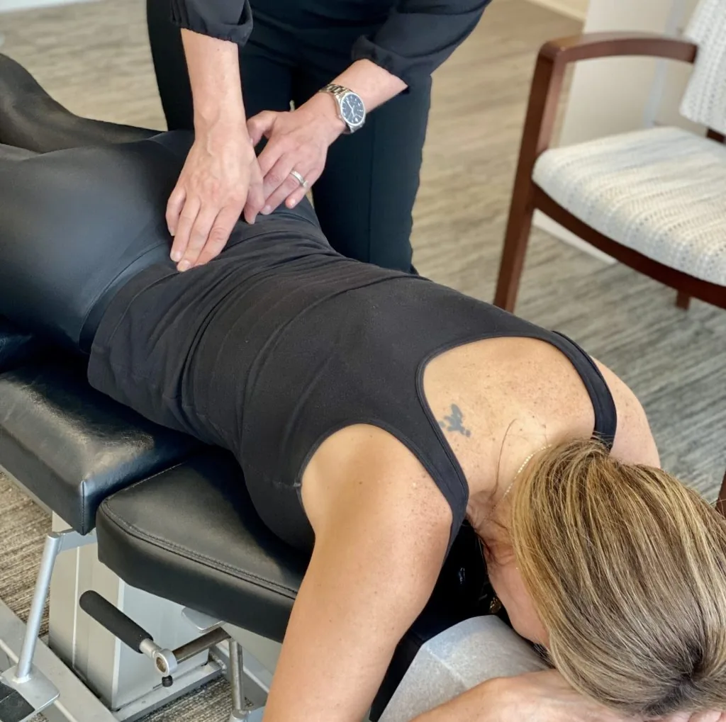 Chiropractor performing a lower-back adjustment on a patient lying face down on a treatment table for back pain.
