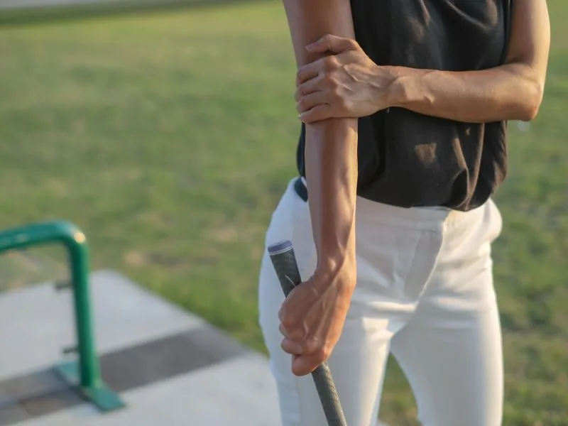 Person holding their forearm near the inner elbow while gripping a golf club, suggesting arm pain after golfing.