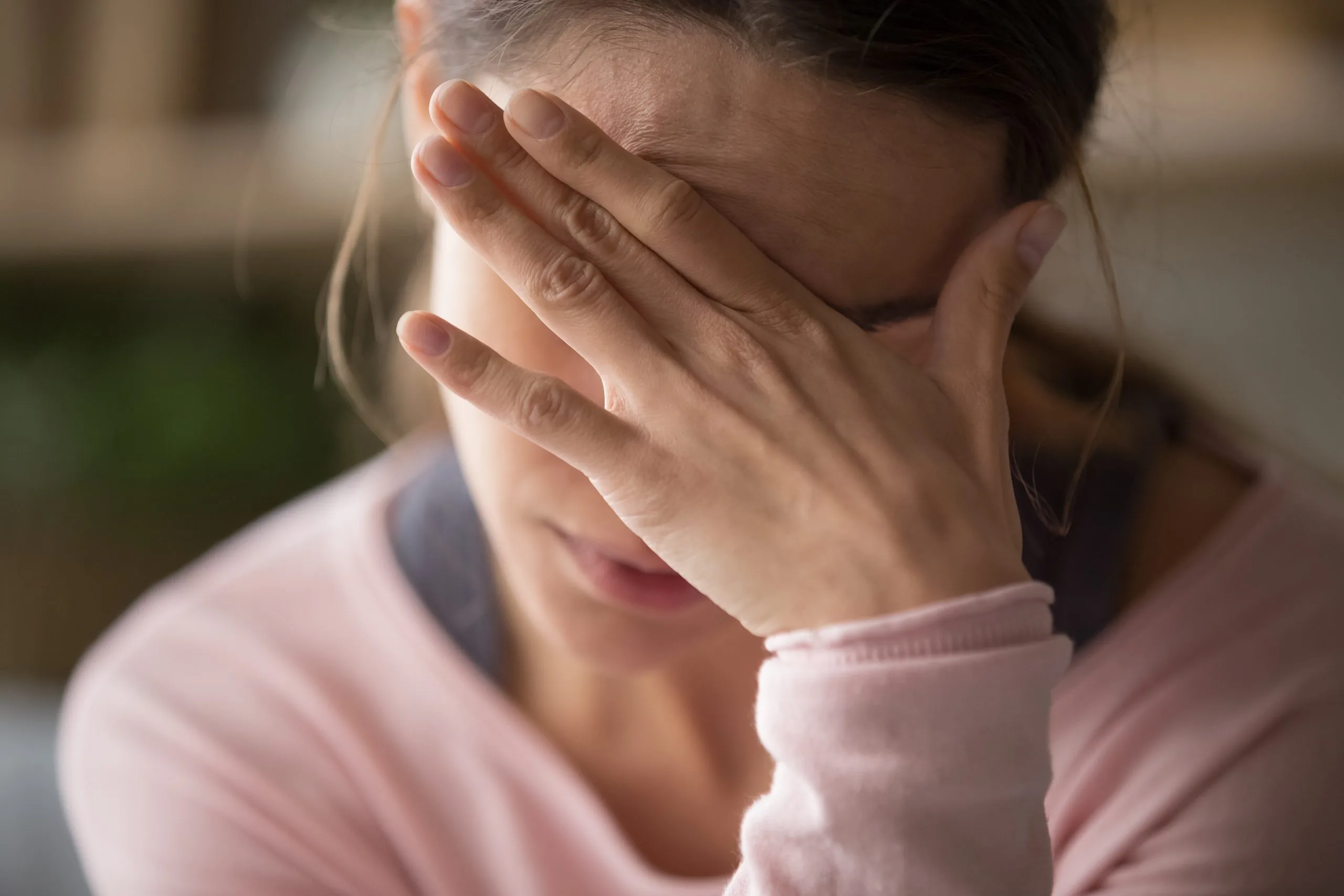 Person covering their face with one hand and pressing their forehead, indicating head pain or a headache.