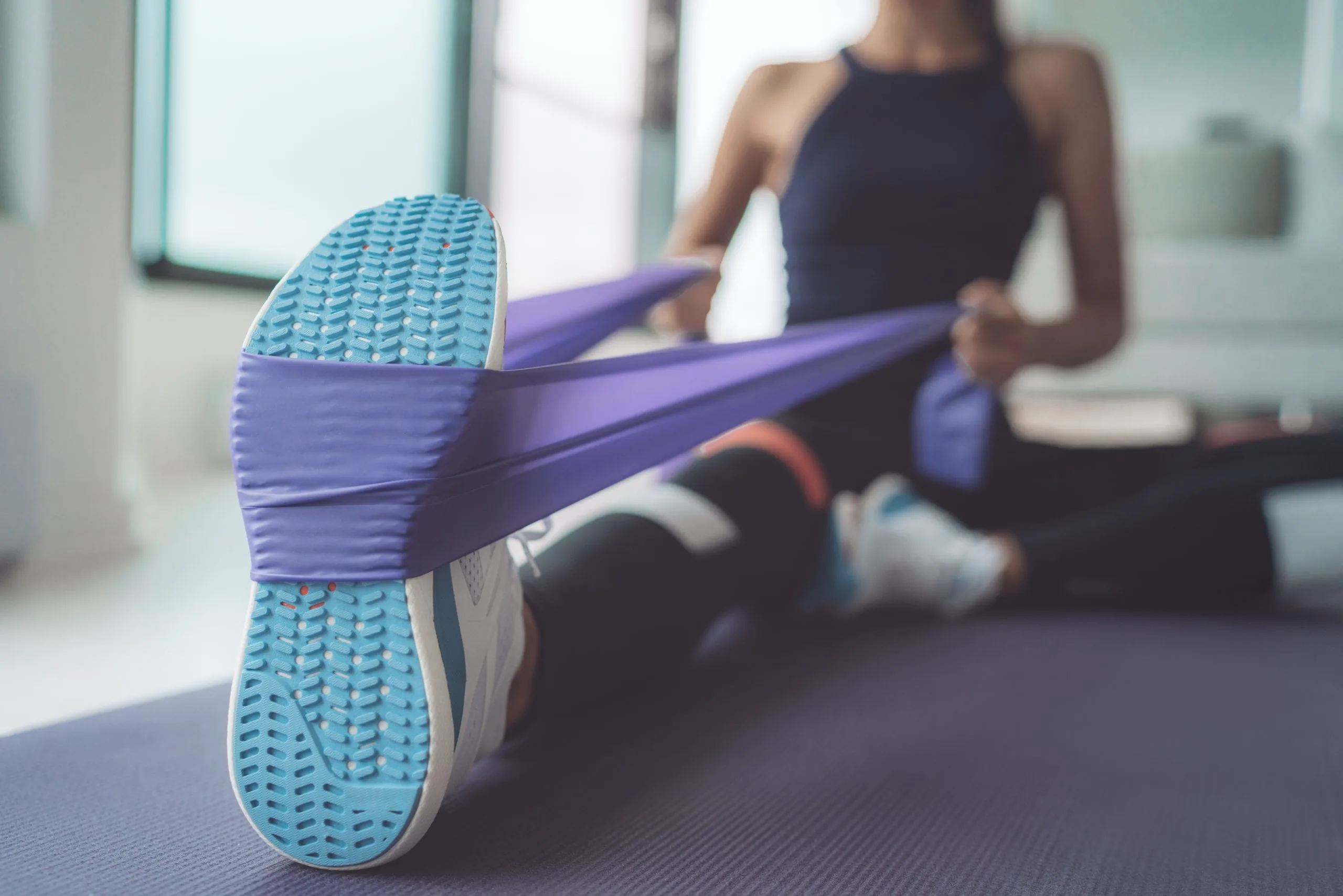 Person using a purple resistance band looped around the foot to perform a seated hip stretch on a mat