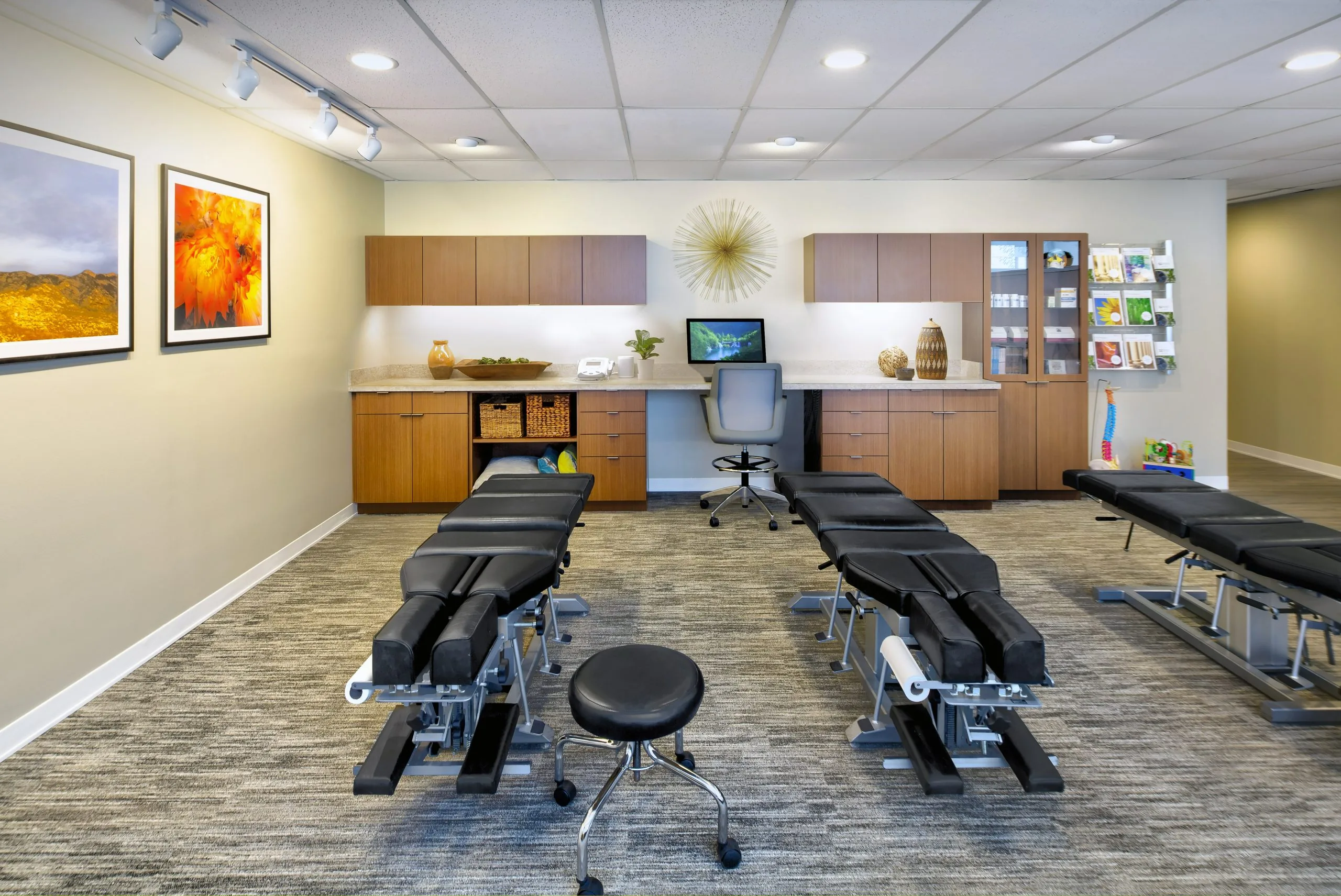 Chiropractic treatment room with multiple adjustment tables, a stool and workstation, set up for knee-pain evaluation and hands-on care.