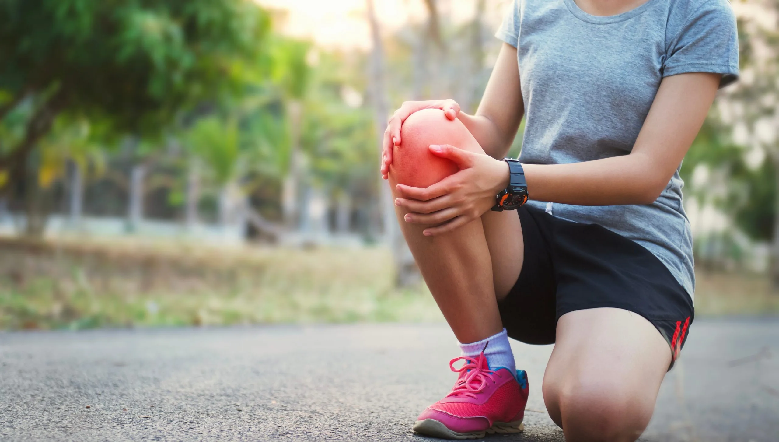 Runner kneeling on a road holding their knee while wearing athletic shoes and shorts