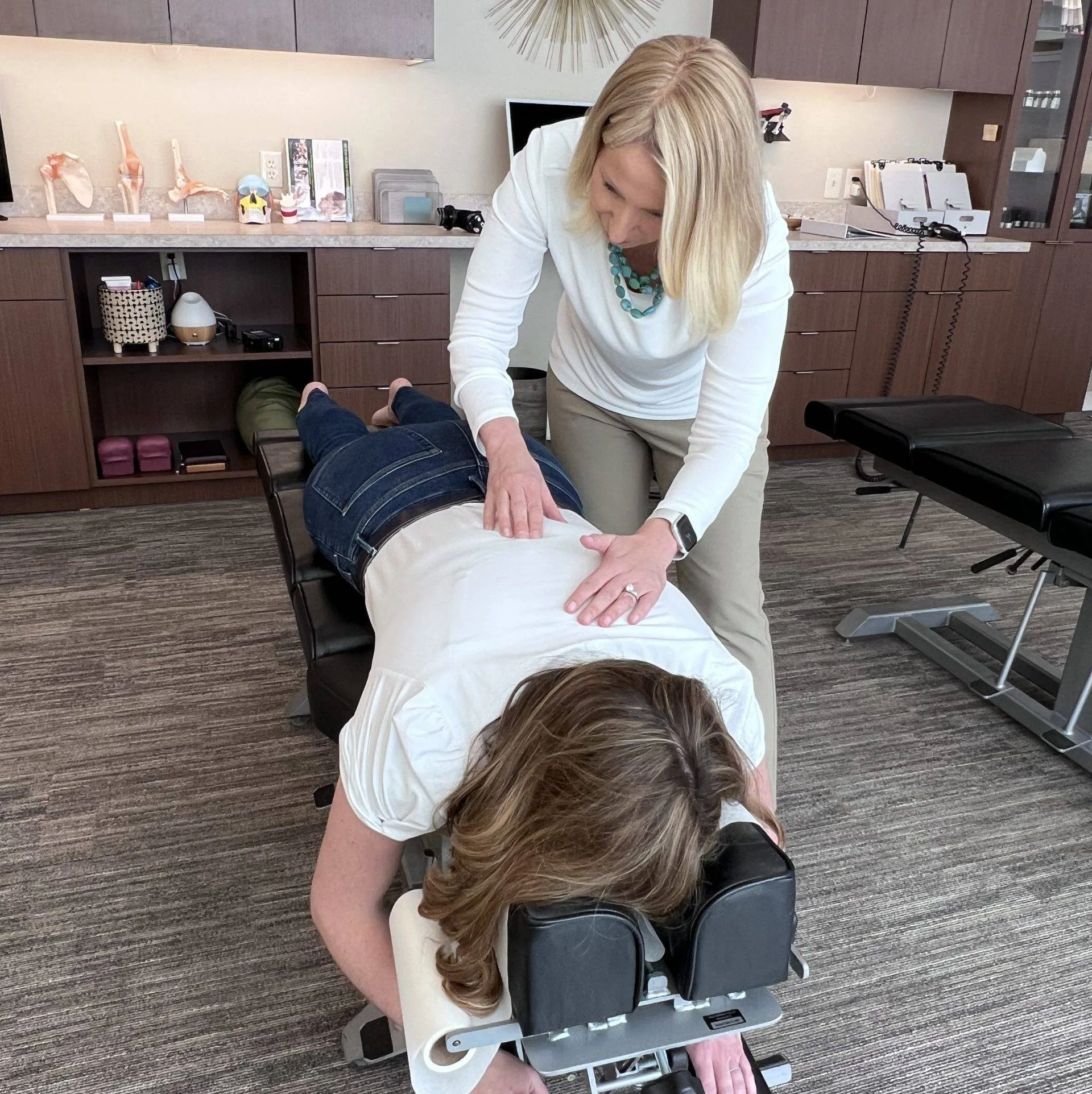 Chiropractor placing hands on a patient's back during an adjustment while the patient lies face down on a treatment table.