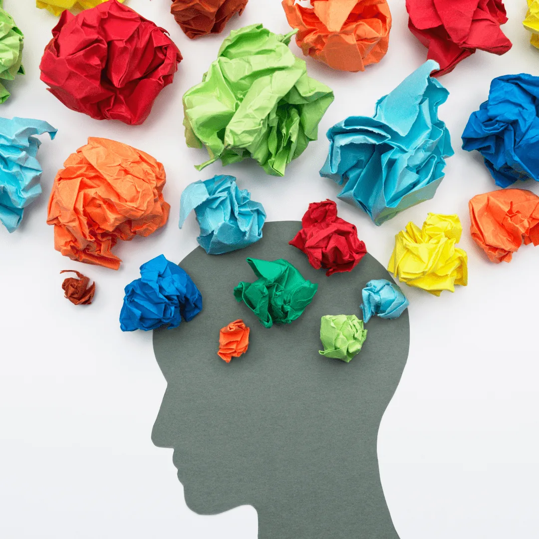 Gray paper silhouette of a head with colorful crumpled paper balls above it representing thoughts or ideas.