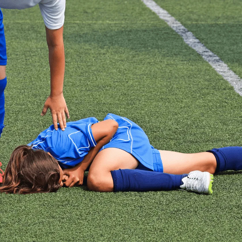 Soccer player lying on turf holding their head as another player reaches down to help