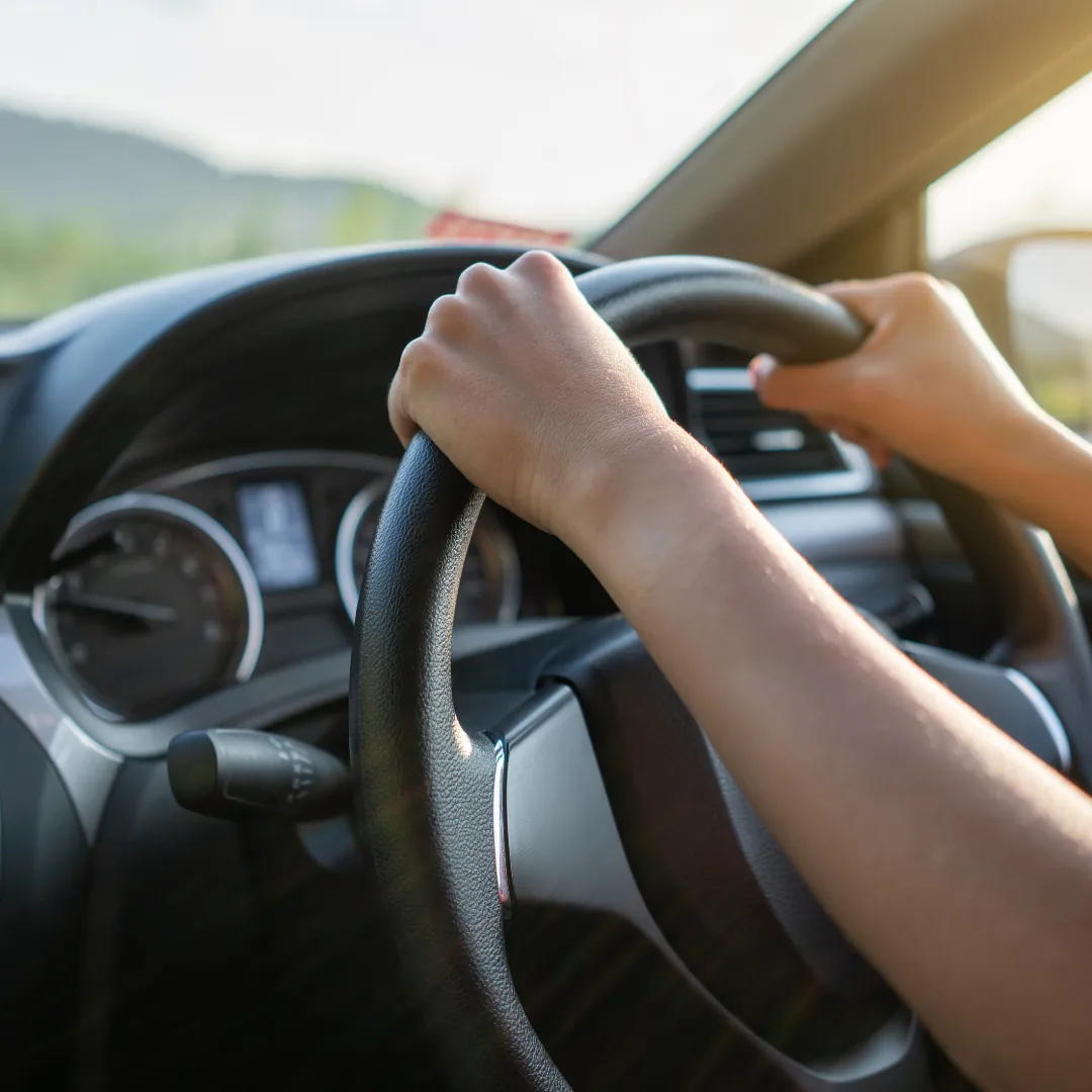 Hands gripping a car steering wheel, viewed from the driver's seat.