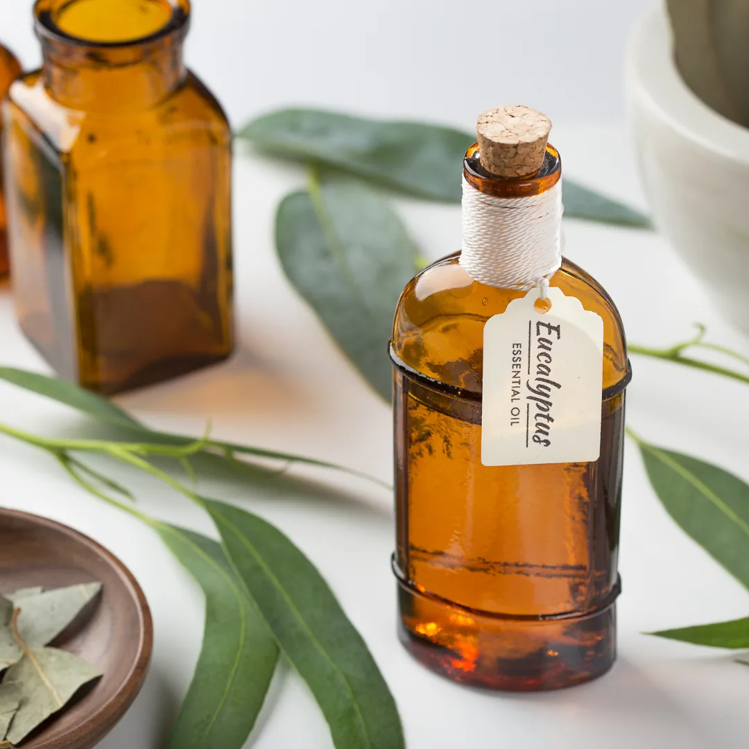 Amber bottle labeled 'Eucalyptus' beside eucalyptus leaves on a white background, an essential oil shown in natural functional-medicine contexts.