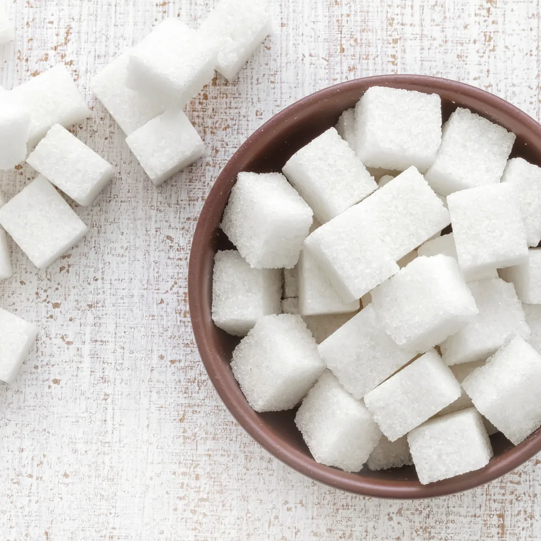 Bowl of white sugar cubes on a textured wooden surface, illustrating sugar consumption often linked to adrenal fatigue.