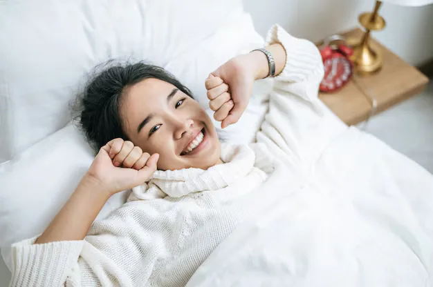 Young woman lying in bed, smiling and stretching as she wakes up