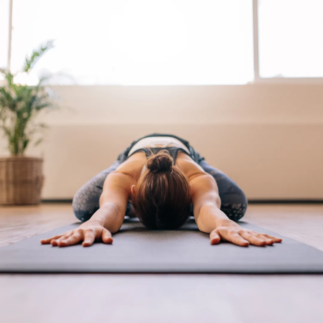Person performing child's pose on a yoga mat in a bright studio, reaching arms forward in a restorative stretch.