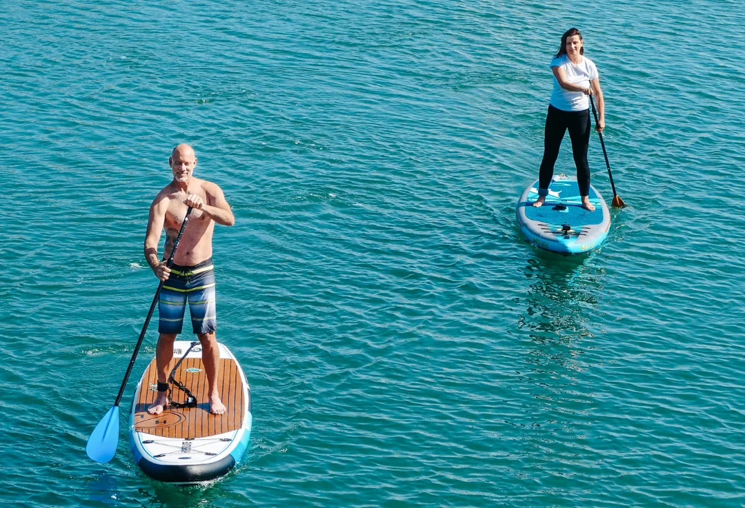 Two people standing on separate paddleboards paddling across calm blue water