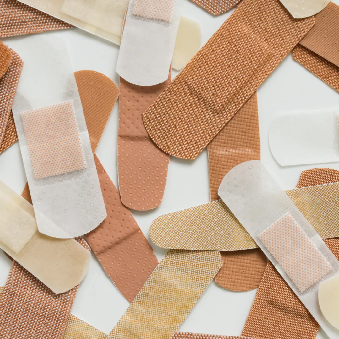 Assorted adhesive bandages in various skin-tone colors scattered on a white surface.