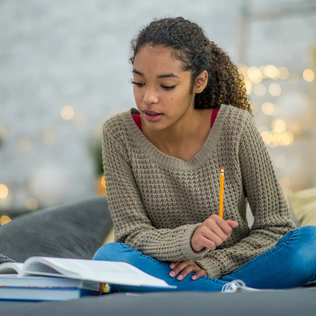Person reading an open textbook while holding a pencil and studying on a couch