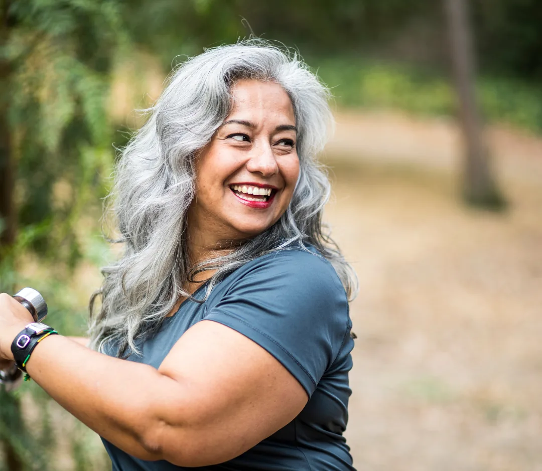 Grey-haired woman smiling outdoors while holding a bicycle handlebar and wearing a fitness tracker