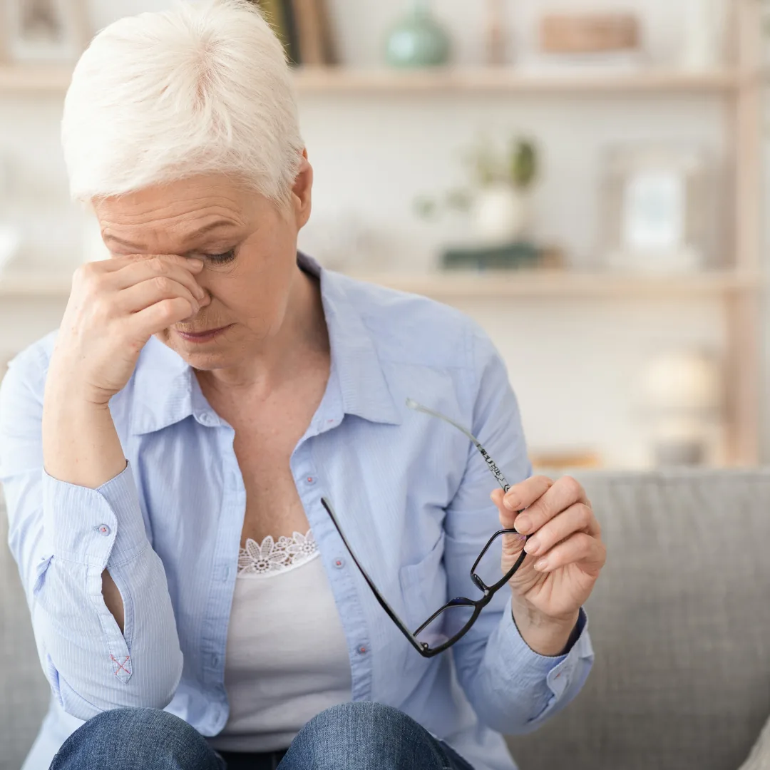 Person holding eyeglasses while rubbing the bridge of their nose