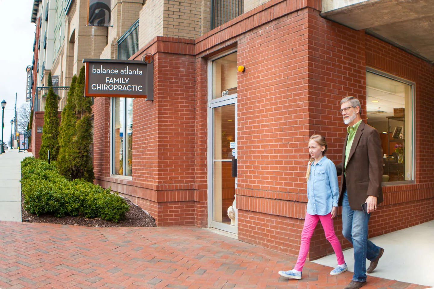 Man and young girl walking past a brick clinic entrance under a sign reading "family chiropractic"