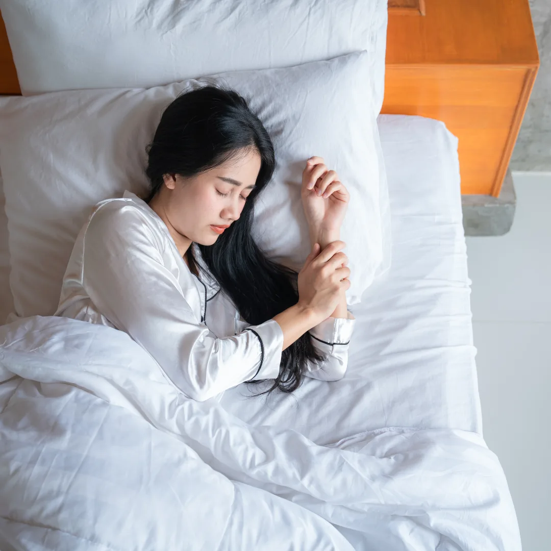 Woman sleeping on her side in white sheets wearing light silk pajamas
