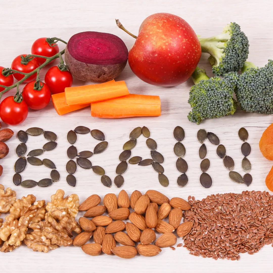 Almonds, walnuts, flax and pumpkin seeds, broccoli, beet, carrot sticks and cherry tomatoes arranged around seeds spelling "BRAIN".