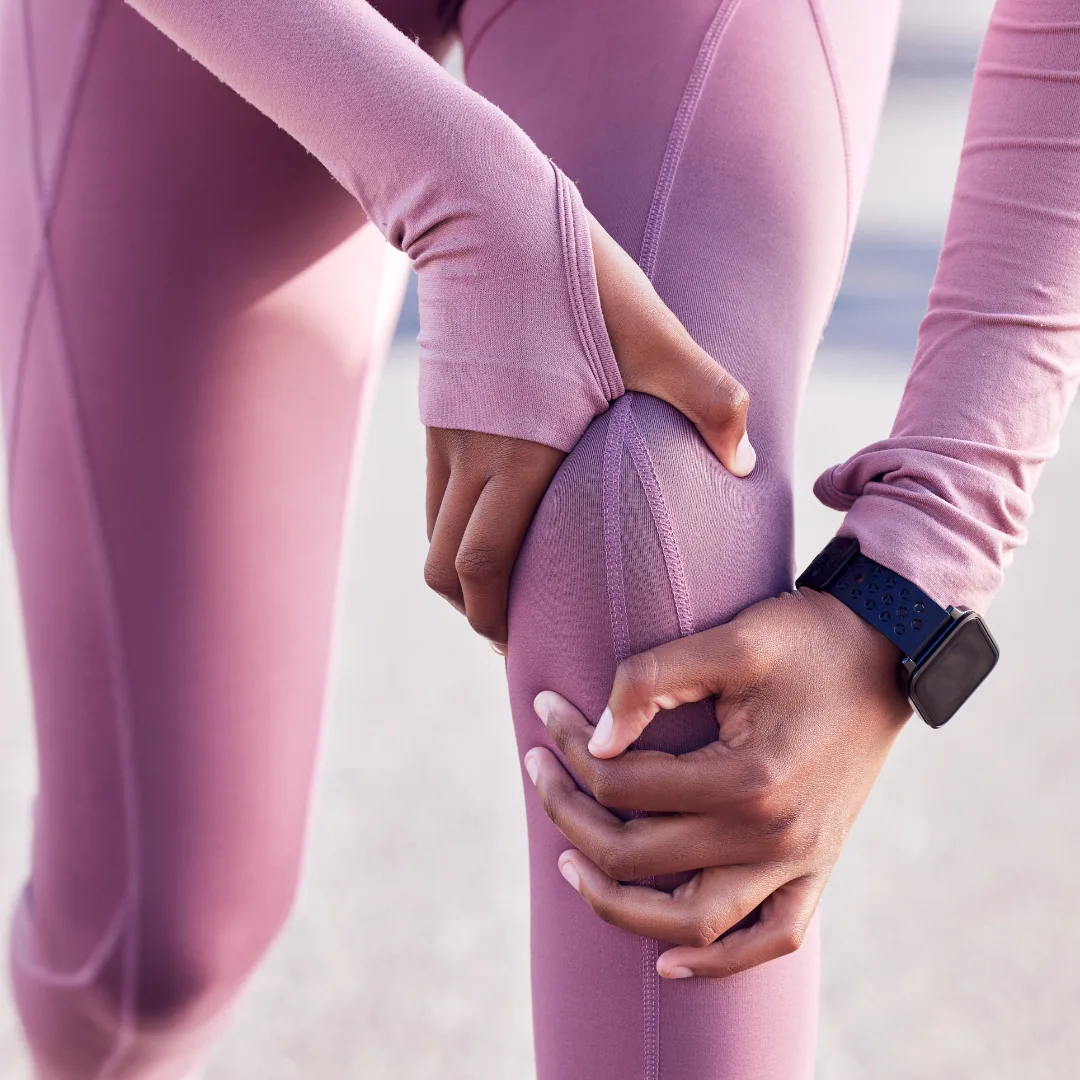 Close-up of hands gripping a knee through mauve workout leggings, smartwatch visible on wrist