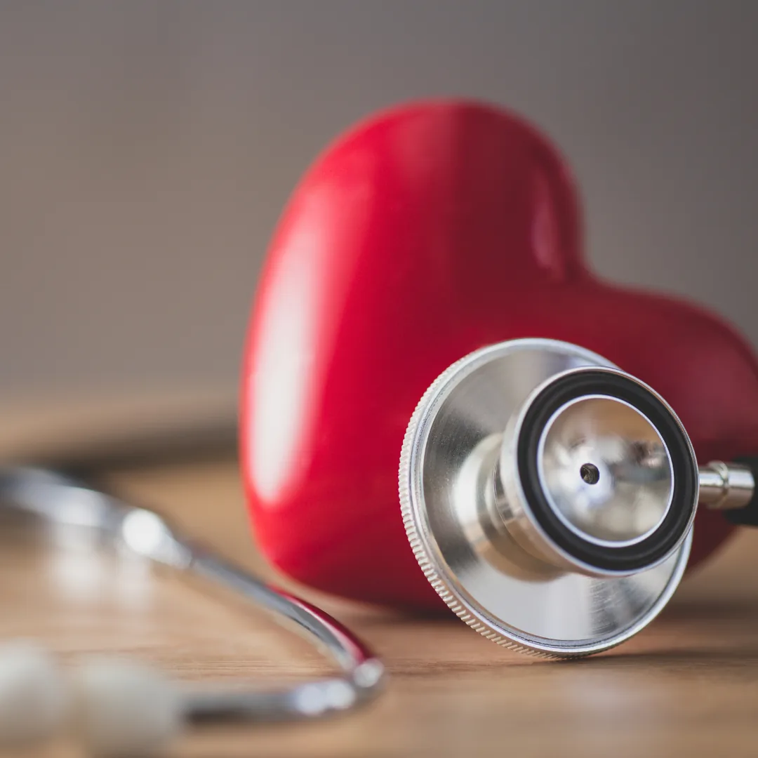 Stethoscope chestpiece resting beside a red heart model on a wooden surface, illustrating cardiovascular checks related to thyroid health.