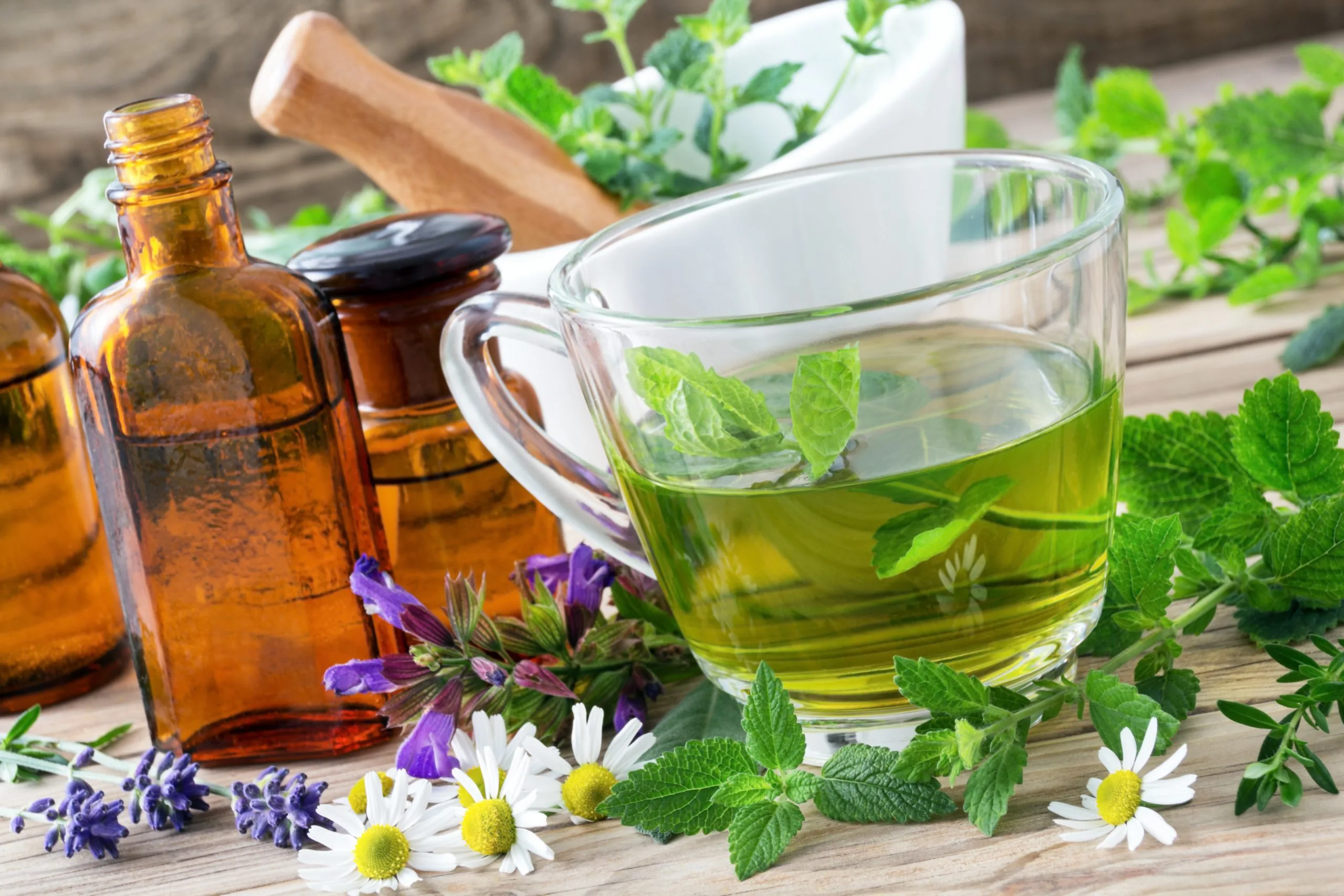 Glass cup of green herbal tea with fresh mint leaves and amber remedy bottles on a wooden table