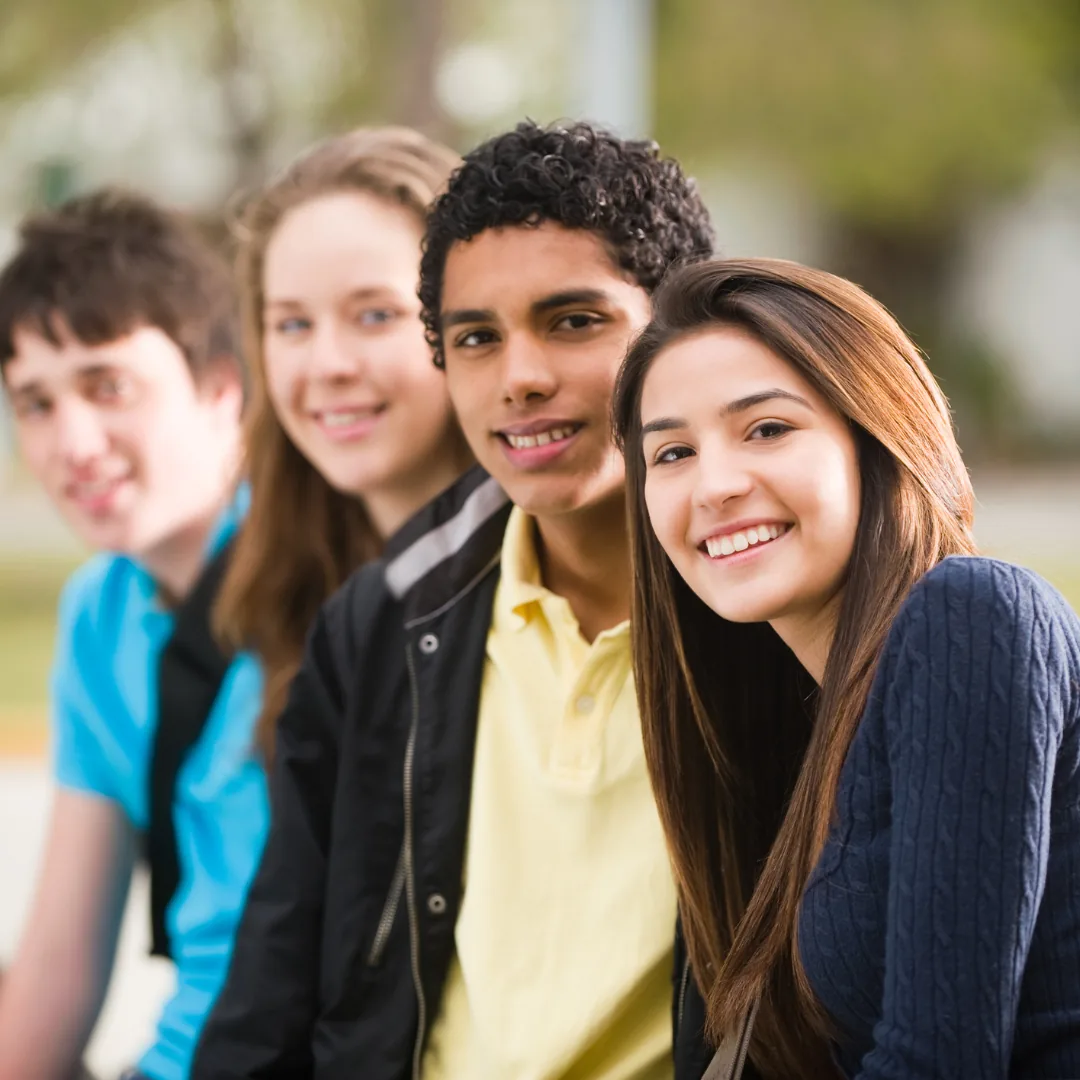 Group of four smiling people seated outdoors in a row, two in clear focus at the right.