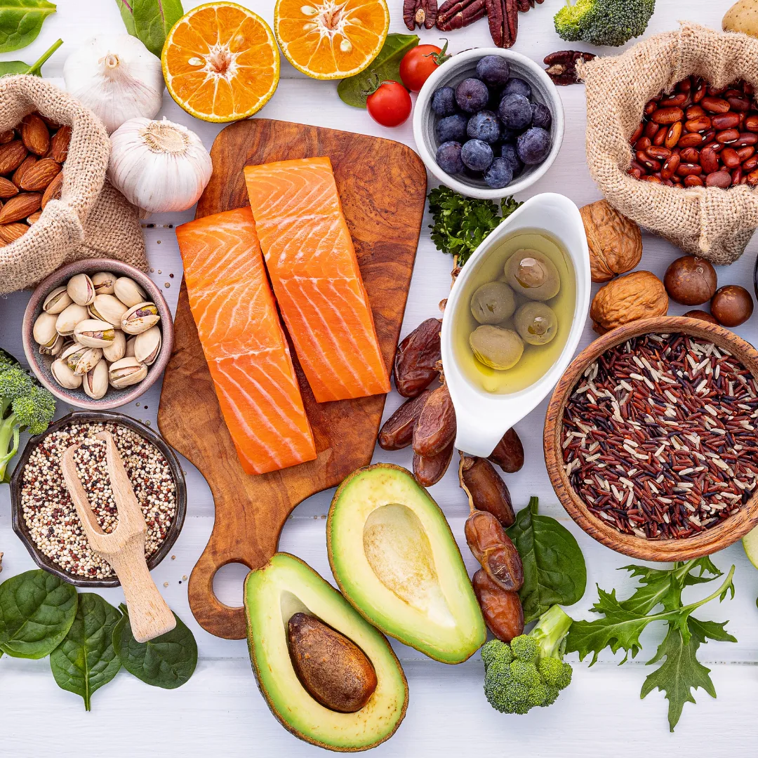 Flat lay of gut-healthy, anti-inflammatory foods including salmon, avocado, olive oil, nuts, blueberries, whole grains, garlic and leafy greens.