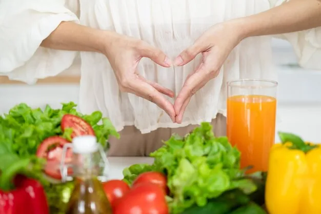 Hands forming a heart shape above a countertop of fresh vegetables, tomatoes, bell peppers, greens, and a glass of orange juice.