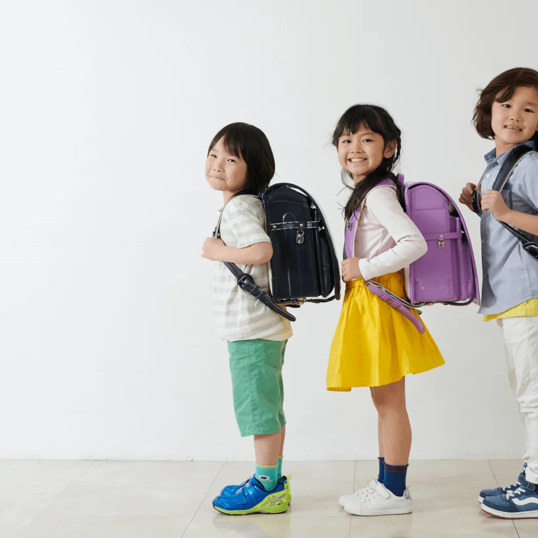 Three children standing in a row wearing school backpacks and smiling