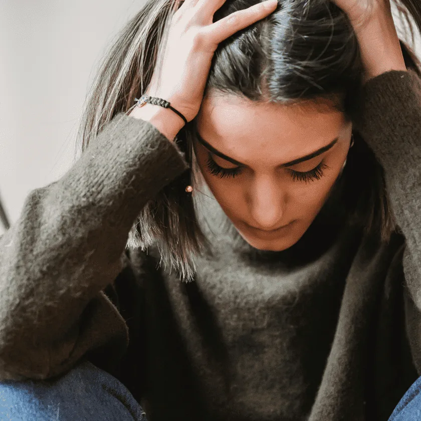 person sitting with hands on their head, looking down