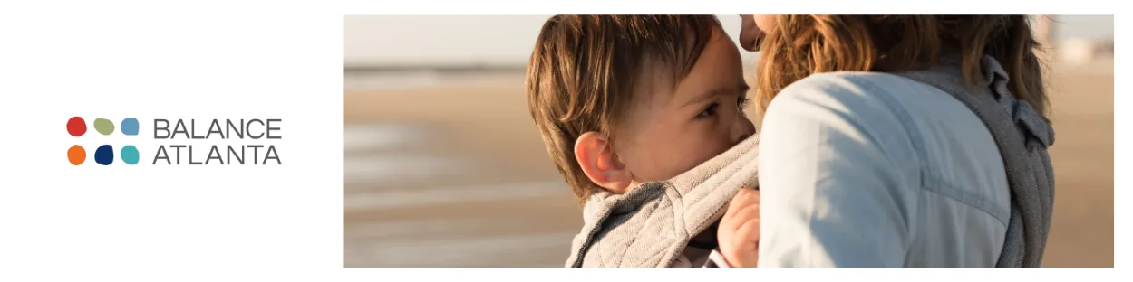 Parent holding a child in a front-facing baby carrier on a beach, with Balance Atlanta logo at left.